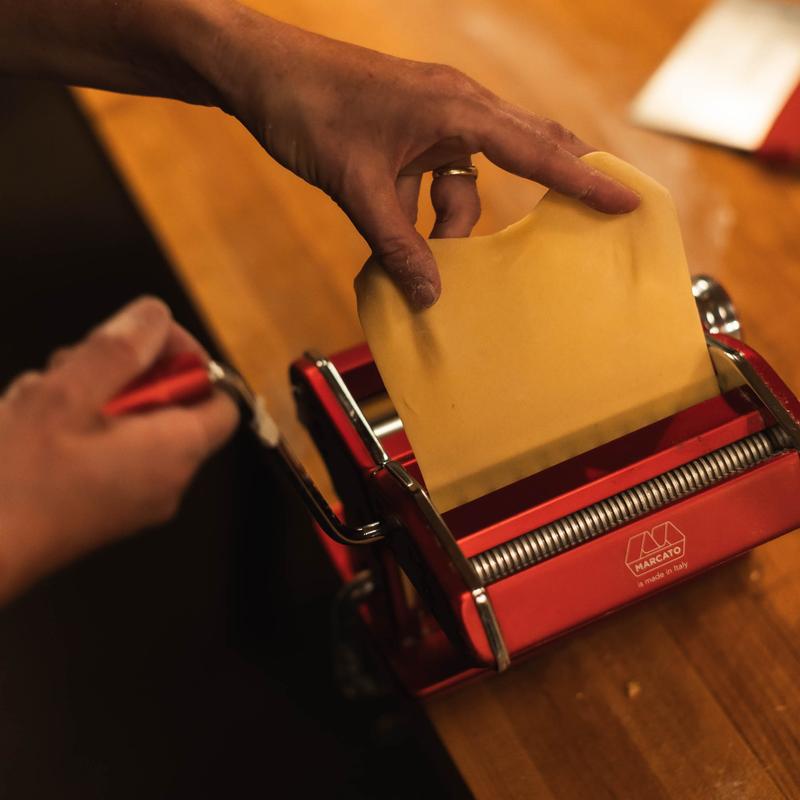 Hands rolling pasta dough through a red pasta machine